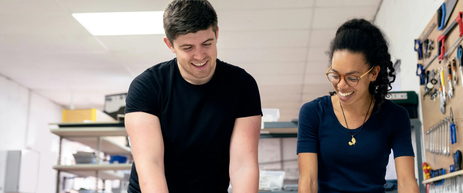 Zwei Kollegen lachen an der Werkbank in einer hellen Werkstatt