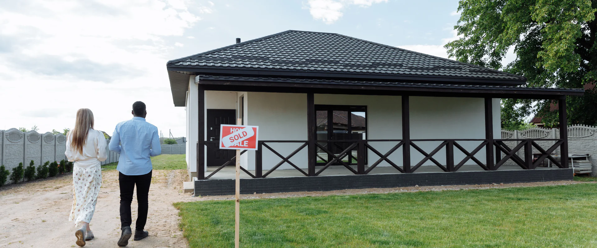 Paar geht auf sein neues Haus mit Verkauft-Schild zu, sonniger Tag