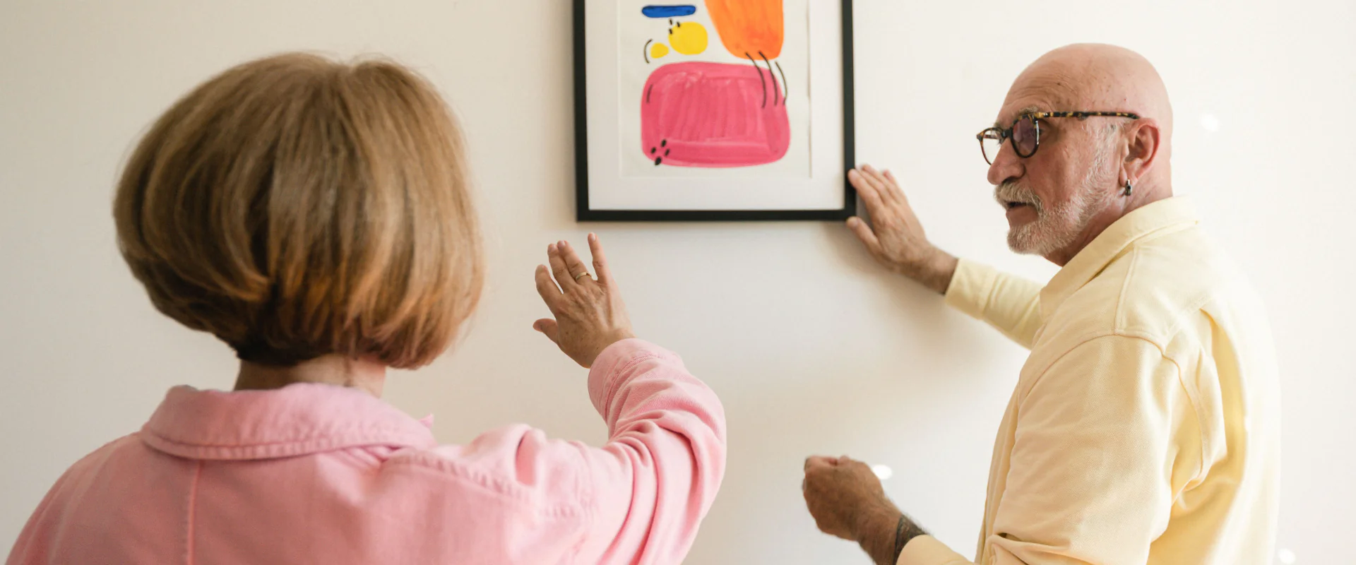 Seniorenpaar hängt in der neuen Wohnung ein buntes Bild auf