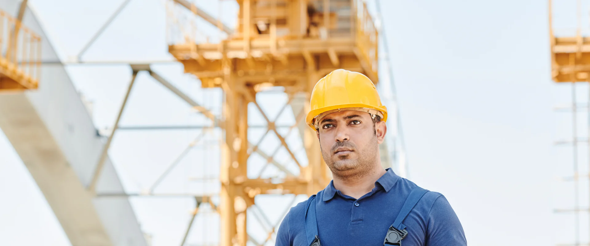 Bauleiter mit Helm und Plan auf einer Großbaustelle vor gelben Kranstrukturen