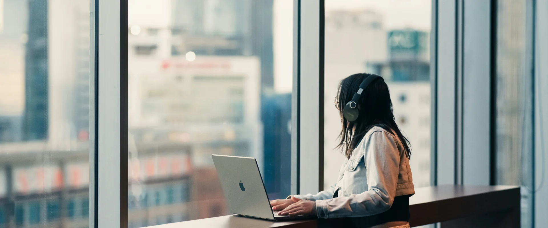 Frau mit Kopfhörern arbeitet am Laptop an einem Stehtisch im Hochhausbüro