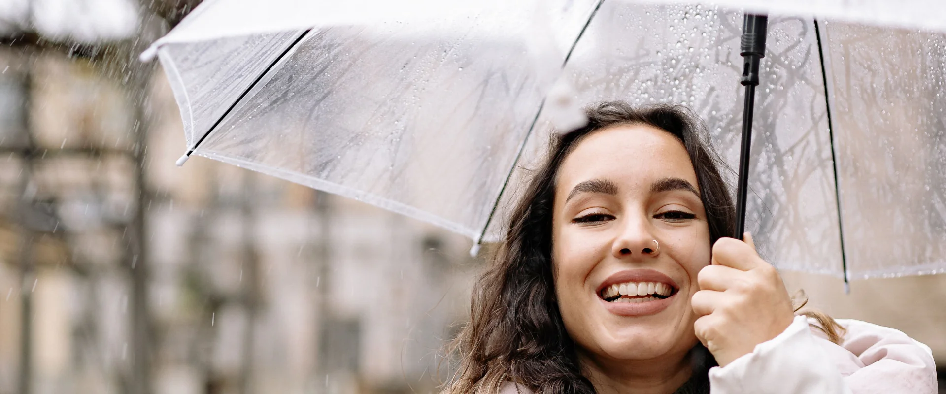 Lächelnde Frau unter einem transparenten Regenschirm an einem Regentag