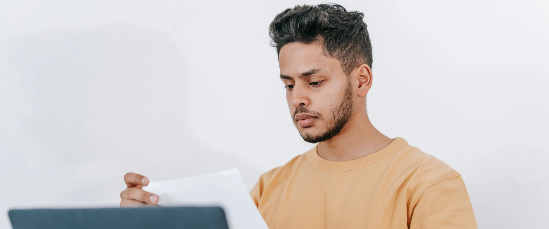 Junger Mann liest am Laptop konzentriert ein Schreiben