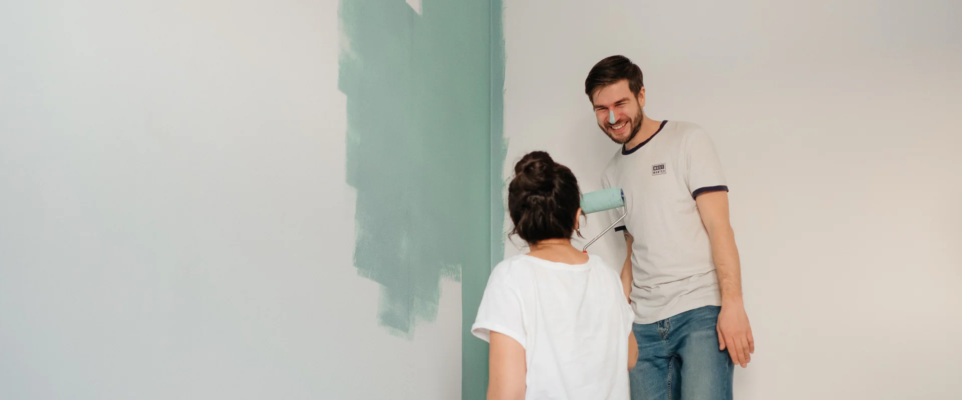 Paar streicht lachend eine Wand in der neuen Wohnung mintgrün
