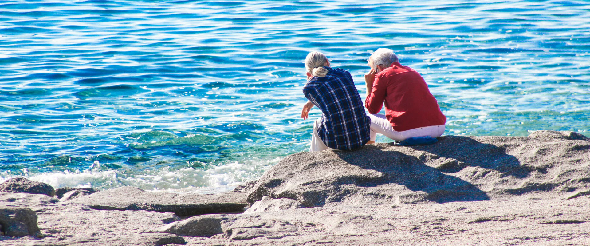 Seniorenpaar sitzt auf Felsen am Meer und blickt aufs Wasser