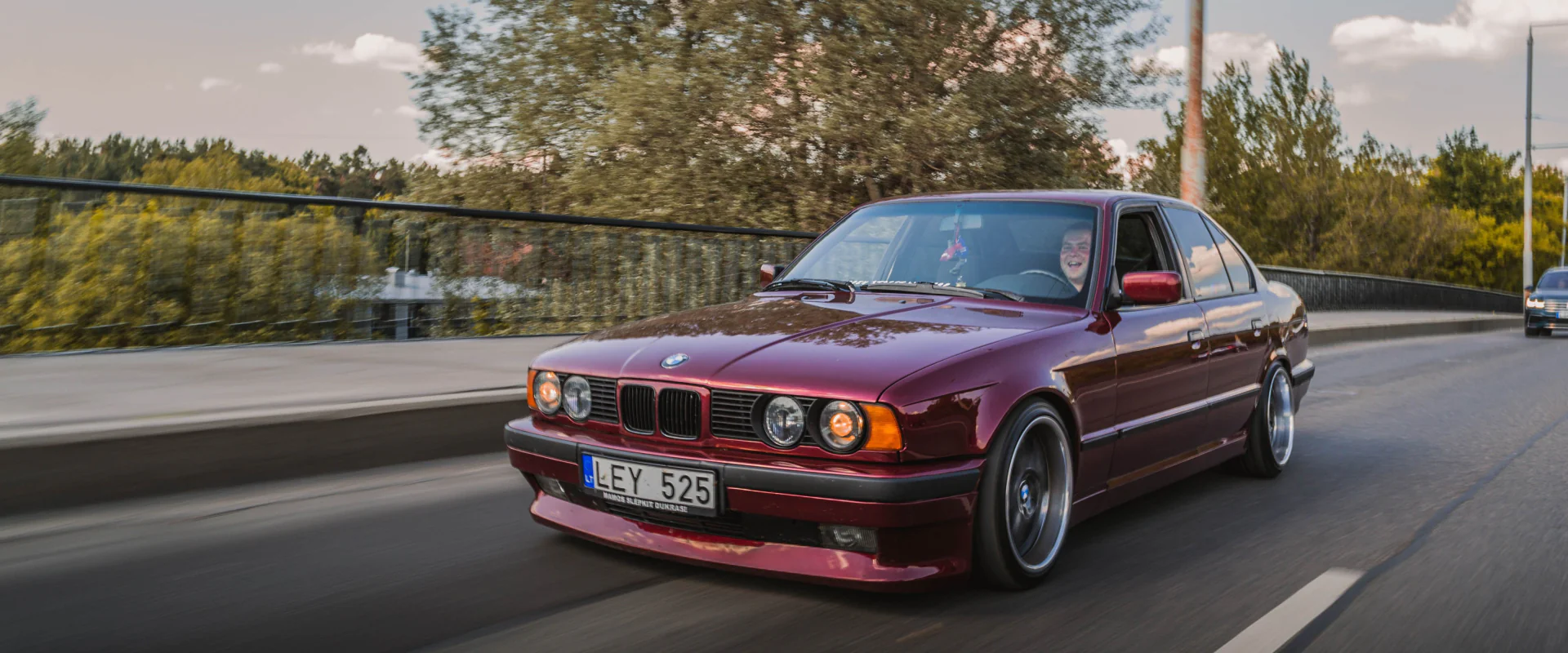 Roter BMW der 5er-Reihe aus den 90ern fährt auf einer Landstraße
